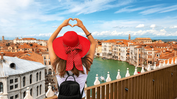 garota fazendo um coração com as mãos de frente para uma cidade italiana