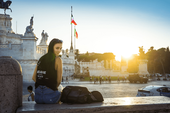 garota sentada em banco olhando para trás em frente a uma praça na itália